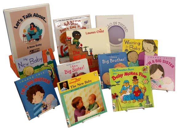Twelve children's picture books and a binder propped on easels. The binder is labeled "Let's Talk About... A New Baby"