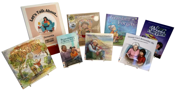 Seven children's picture books and a binder propped on easels. The binder is labeled "Let's Talk About... Dementia"